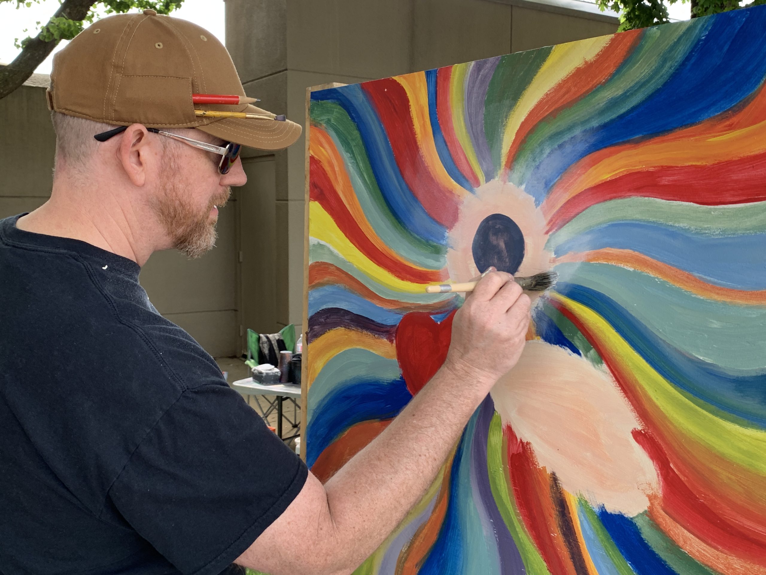 A man wearing a tan hat paints a picture at Artsfest